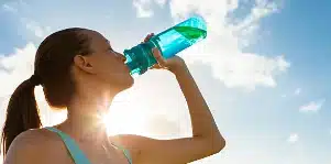 Femme s'hydratant en plein air avec une gourde, sous le soleil