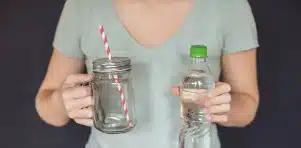 Personne tenant une bouteille d’eau et un verre vide avec une paille